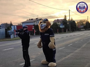 policjant Ogniwa Ruchu Drogowego podczas pomiaru prędkości, obok niego stoi maskotka dolnośląskiej Policji - Komisarz Lew