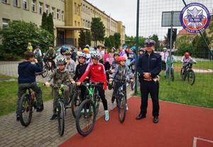 policjant z Ogniwa Ruchu Drogowego oławskiej jednostki podczas grupowego zdjęcia z uczniami zdającymi praktyczny egzamin na kartę rowerową