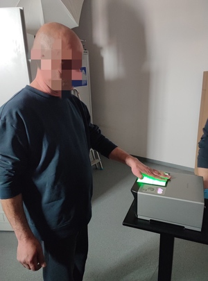 na zdjęciu widać zatrzymanego mężczyznę, któremu technik kryminalistyki pobiera odciski palców