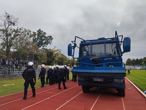 policjanci stoją na murawie stadionu miejskiego w Oławie, obok nich stoi armatka wodna