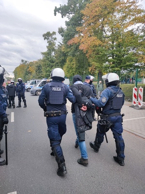 policjanci z Oddzialów Prewencji Policji Komendy Wojewódzkiej Policji we Wrocławiu ulicą prowadzą zatrzymanego kibica, który ma założone kajdanki na ręce trzymane z tyłu