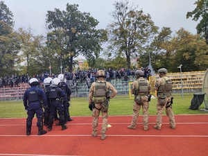 policjanci z Oddziałów Prewencji Policji Komendy Wojewódzkiej policji we Wrocławiu wspólnie z funkcjonariuszami ze SPAP stoją na stadionie przy trybunach kibiców przyjezdnych