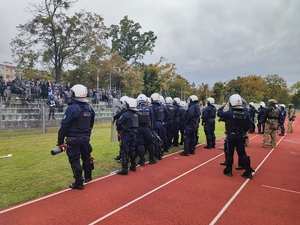 policjanci w mundurach oraz pz stoją przy trybunach kibiców przyjezdnych