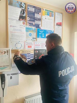 policjant z Rewiru Dzielnicowych rozwiesza plakat dotyczący rekrutacji do policji