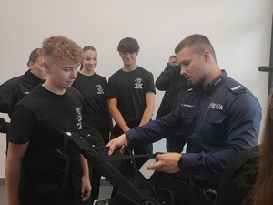 policjant tłumaczy uczniom zasady zadania założenia sprzętu PZ na czas