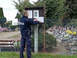 policjant rozwiesza przy cmentarzu policyjne klepsydry z apelem