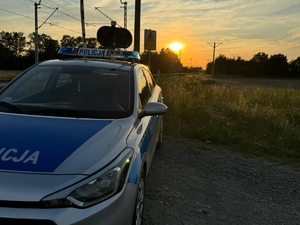 oznakowany radiowóz policyjny zaparkowany przy przejeździe kolejowym