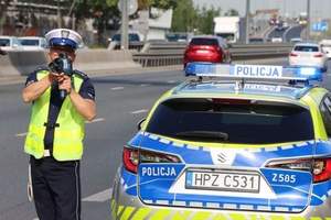 policjant ruchu drogowego stojący przy oznakowanym radiowozie podczas kontroli prędkości