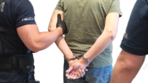 Mężczyzna w kajdankach trzymany pod ramię przez policjanta