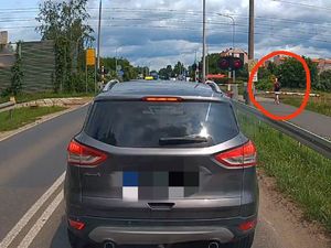 zdjęcie samochodu oraz znajdującego się po prawej stronie pieszego (oznaczonego w kółku), który przechorzi przez tory na czerwonym świetle, omijając zamknięte rogatki