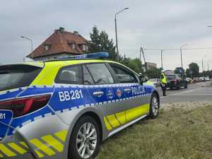 oznakowany policyjny radiowóz, w tle policjantka kierująca ruchem
