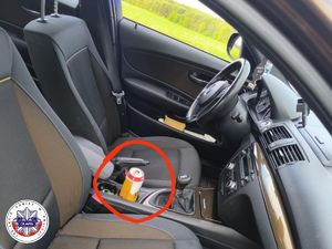 wnętrze samochodu marki bmw z zaznaczeniem w czerwonym kole puszki po piwie znajdującej się w stojaku na napoje