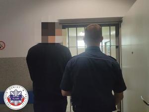 policjant prowadzi do pomieszczenia dla osób zatrzymanych aresztowanego mężczyznę