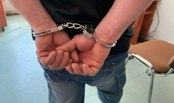 mężczyzna mający założone kajdanki na ręce trzymane z tyłu