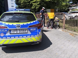 policyjny oznakowany radiowóz i policjant podczas kontroli drogowej rowerzysty