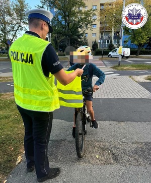 policjant przekazujący chłopcu jadącemu rowerem kamizelkę i opaskę odblaskową