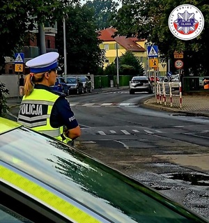 policjantka przy radiowozie kontrolująca okolice przejść dla pieszych w rejonie szkół