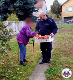 Policjant niosący skrzynkę jabłek dla seniorki