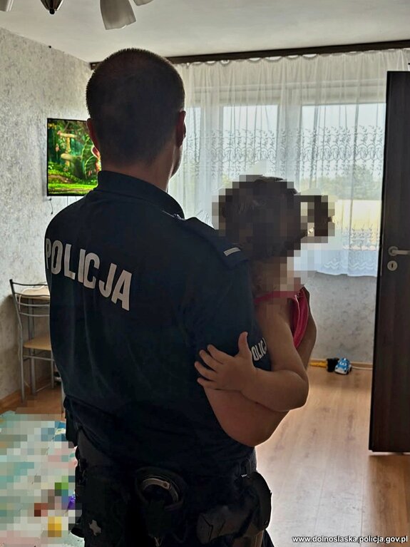 Policjant trzymający na rękach 2-letnią dziewczynkę