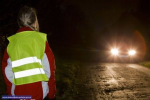 dziecko w kamizelce odblaskowej na tle nadjeżdżającego samochodu